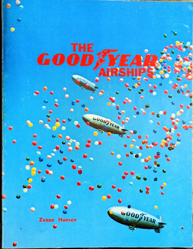 Picture of book cover showing 3 airships flying in a bright blue sky amongst hundreds of colourful toy balloons.
